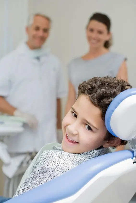 A smiling child in the dental chair with dentist and nurse
